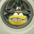 Close-up of a yellow shoe washing bag with white sneakers inside, securely zipped in a washing machine drum, demonstrating it
